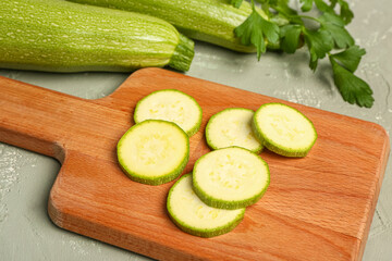 Board with slices of fresh zucchini and parsley on grey background
