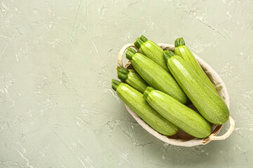 Basket with many fresh green zucchini on grey background