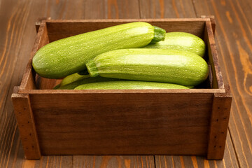 Box with fresh green zucchini on wooden background