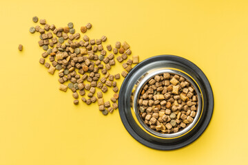 Dry kibble pet food. Dog or cat food in bowl on yellow background. Top view.