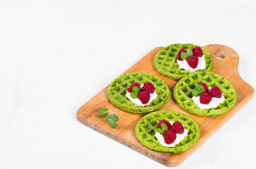 Vegan Round Spinach waffles with cream and raspberries, on a serving wooden board. White background. Copy space