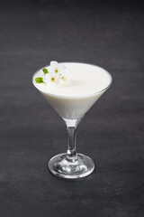 Vanilla cream dessert, Panna Cotta, decorated with small white flowers, in a martini glass. Dark gray background