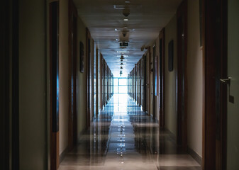 Dark long corridor in hotel with many doors and light in end from big window.