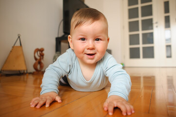 Portrait of cute happy smiling baby boy crawls on the home floor and looking at camera. Joy and happiness concept. Love and family emotion