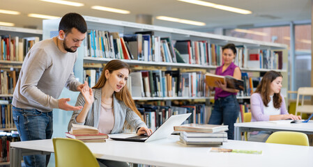 Dissatisfied young female student showing stop gesture to annoying male friend at library of...