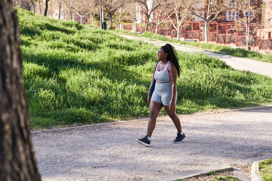 young African American woman in sportswear walking through a city park on her way to the gym to work out.