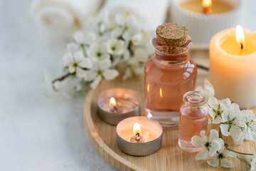 Fototapeta na wymiar Burning candles, spa setting, essential oils, organic pure aromatic ingredients, atmosphere of relax. Aromatherapy, cozy home decor concept. Perfumery bottles, elegant composition with spring flowers