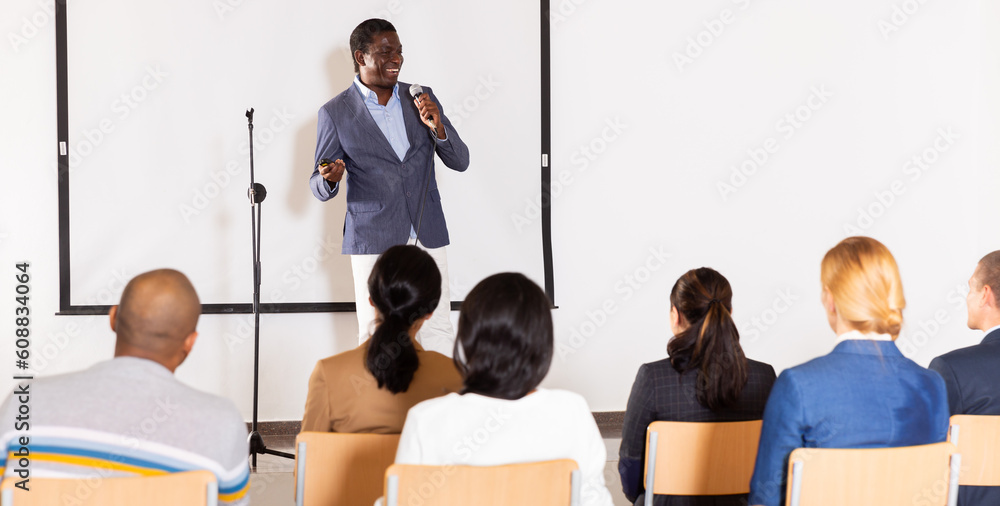 Wall mural positive african american with microphone speaking at corporate business event in conference room