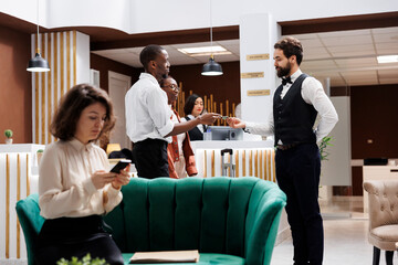 Hotel concierge taking cash from man, accepting to carry suitcases and help with bags after registration at front desk. Young adult working as porter at luxury resort, receiving money tip.