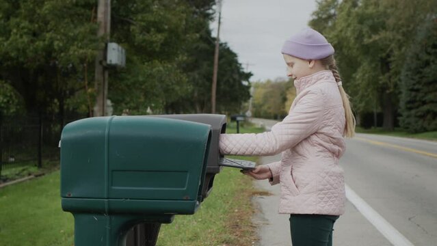 A child picks up letters from a street mailbox in a US suburb. Side view