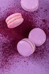 Obraz na płótnie Canvas Pastel colored sweet french macaroons and splash of dry blueberry powder on purple background. Beautiful composition for bakery and pastry shop, top view