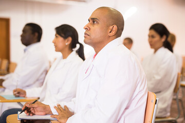 Focused Hispanic man participating in medical congress with colleagues, listening attentively to...