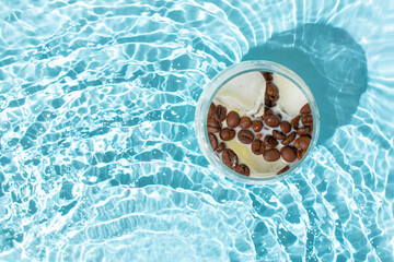 Glass of ice cubes with coffee beans and milk isolated in rippled water. Cold fresh coffee concept....