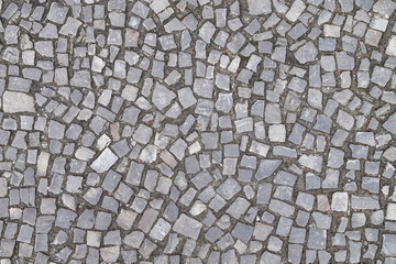 Texture of an old stoneblock pavement cobbled with gray stone tiles of different shapes as a background