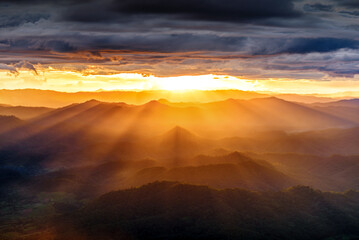 amazing dramatic cloudscape in sunset with sun rays over misty mountains landscape