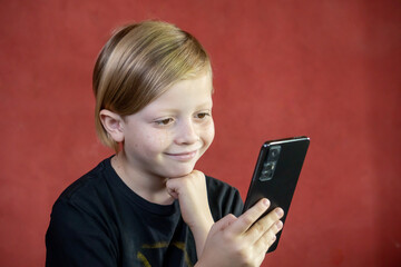 Niño mirando celular rubio con fondo rojo