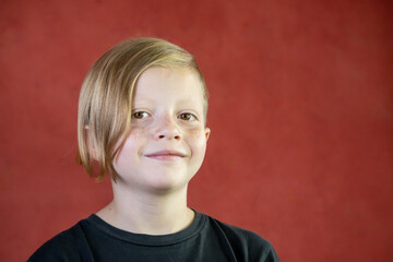 Retrato de niño rubio con peinado moderno en fondo rojo 