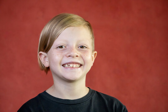 Niño feliz rubio de pelo lacio con fondo rojo