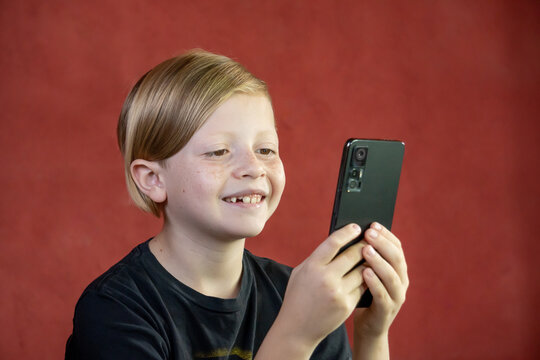 Niño con teléfono móvil sonriente y feliz con fondo rojo 