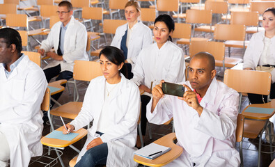 Fototapeta na wymiar Portrait of interested hispanic doctor attending refresher course, using smartphone to record lecture