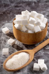 Fototapeta na wymiar White sugar cubes in wooden bowl and granulated sugar on wooden spoon.