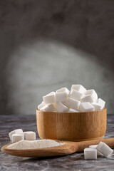 Fototapeta na wymiar White sugar cubes in wooden bowl and granulated sugar on wooden spoon.