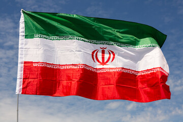 Big flag of Iran fastened on stick against background of blue sky under daylight