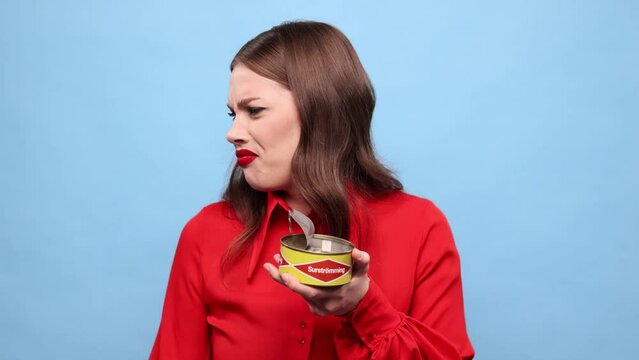 Emotional young girl eating traditional swedish dish - salted fermented herring against blue background. Concept of taste, human emotions, facial expression. Swedish cuisine