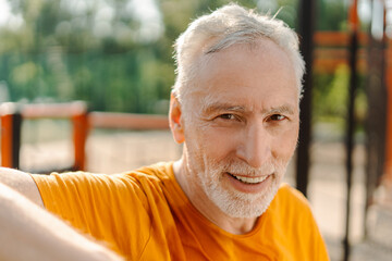 Headshot handsome senior man athlete smiling, looking at camera, standing over blurred sportsground