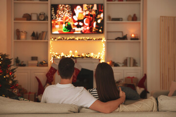 Couple watching Christmas movie via TV in cosy room, back view. Winter holidays atmosphere