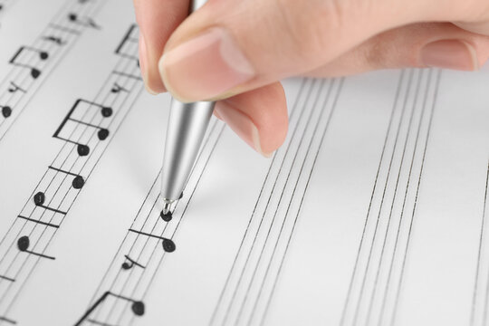 Woman writing musical notes with pen on sheet of paper, closeup