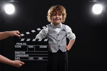 Smiling cute boy performing while second assistant camera holding clapperboard on stage. Little...