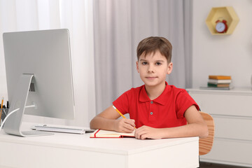 Naklejka premium Boy writing in notepad while using computer at desk in room. Home workplace