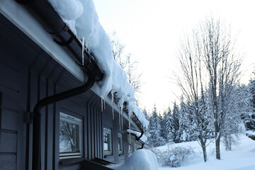 Beautiful view of wooden house with icicles near snowy trees and bushes on winter day - obrazy, fototapety, plakaty