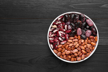 Different kinds of dry kidney beans in bowl on wooden table, top view. Space for text