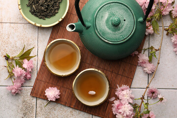 Traditional ceremony. Cup of brewed tea, teapot, dried leaves and sakura flowers on tiled table,...
