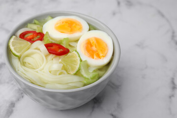Bowl of delicious rice noodle soup with celery and egg on white marble table, closeup. Space for text