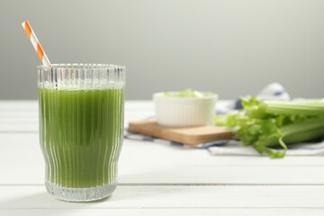 Glass of celery juice and fresh vegetables on white wooden table, space for text
