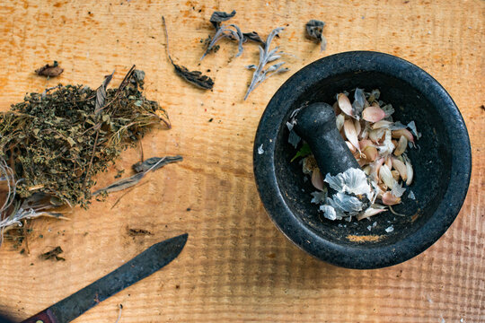 herbs, a garlic filled black molcajete and a rustic knife on a wood board