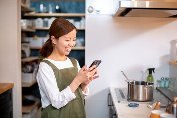 キッチンでスマホを見る、エプロン姿の若い日本人の女性