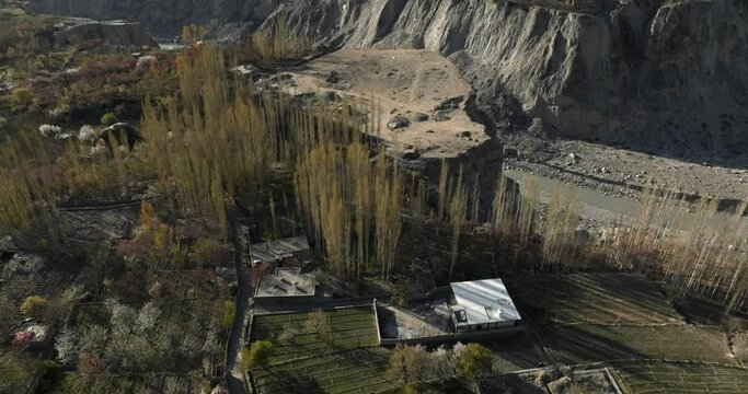 An aerial view of a village and fields during blossom, with an amazing cliff in the Hunza Valley of the Karakoram range in the Himalayas, Gilgit Baltistan, Pakistan.