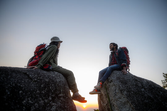 Hikers with backpacks relaxing on top of a mountain and enjoying the view of valley at sunset