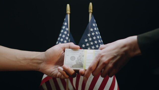 Latino Hand Gives Stack of Money to Caucasian Hand in Exchange for Passport, In Front of 2 USA Flags. Shot with ARRI Alexa in ArriRaw at 120 fps, exported 23.98 fps QuickTime Apple ProRes 422 HQ.