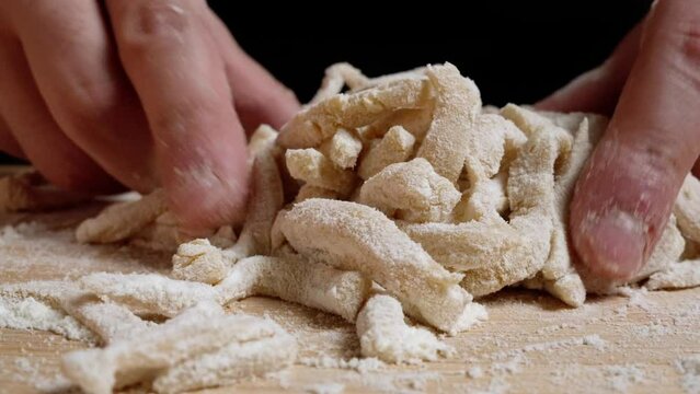 preparing a pasta by rotating and mixing it with flour on a wooden board with a black background