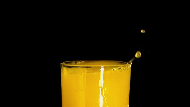 ice qube falling into orange juice glass and making splashes slow motion with black background