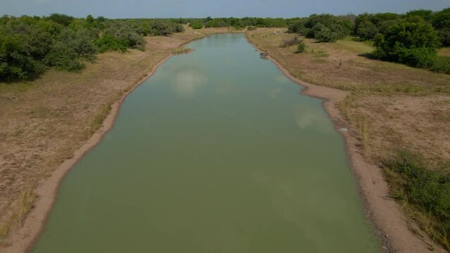 A lake in the middle of the bush in Africa, from a drone. The lake is half dry, in the middle of a desert patch, with trees surrounding the sand