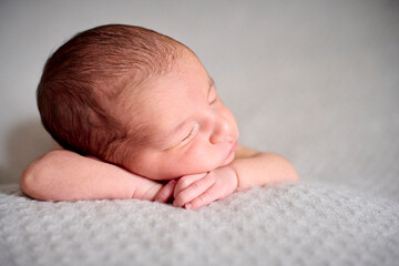 A naked newborn sleeping on her hands on top of a gray blanket