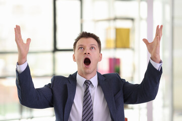 Excited businessman screams and raises hands up in office
