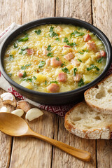 Soup kulesh with millet, potatoes and bacon in a black bowl on a wooden table closeup. Vertical