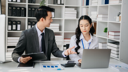 Asian business colleague business presents and explains and using laptop and tablet. Teamwork, financial marketing team, while sitting in office room.